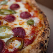 Close-up of a pizza with pepperoni and green peppers on a wooden surface