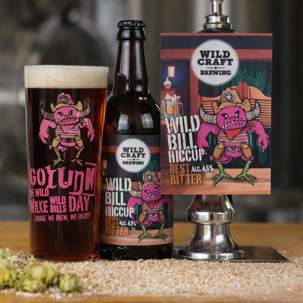 Wildcraft Brewing beer bottle, glass, and tap handle on a wooden surface with hop cones.