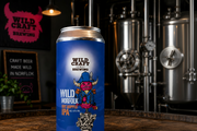 Can of Wild Craft Brewing Wild Norfolk Dry Hopped IPA on a wooden surface with brewing equipment in the background.