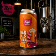 Can of Wild Craft Lager on a wooden surface with brewing equipment in the background