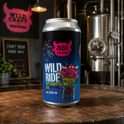 Beer can with 'Wild Craft Brewing' branding on a wooden table in a brewery setting.