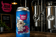 Can of Wildcraft Brewing Wilder Winter Dark Malt beer on a wooden surface with brewery equipment in the background.