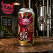 Can of Wild Craft Brewing Wild to the Core Cider on a wooden surface with brewing equipment in the background.